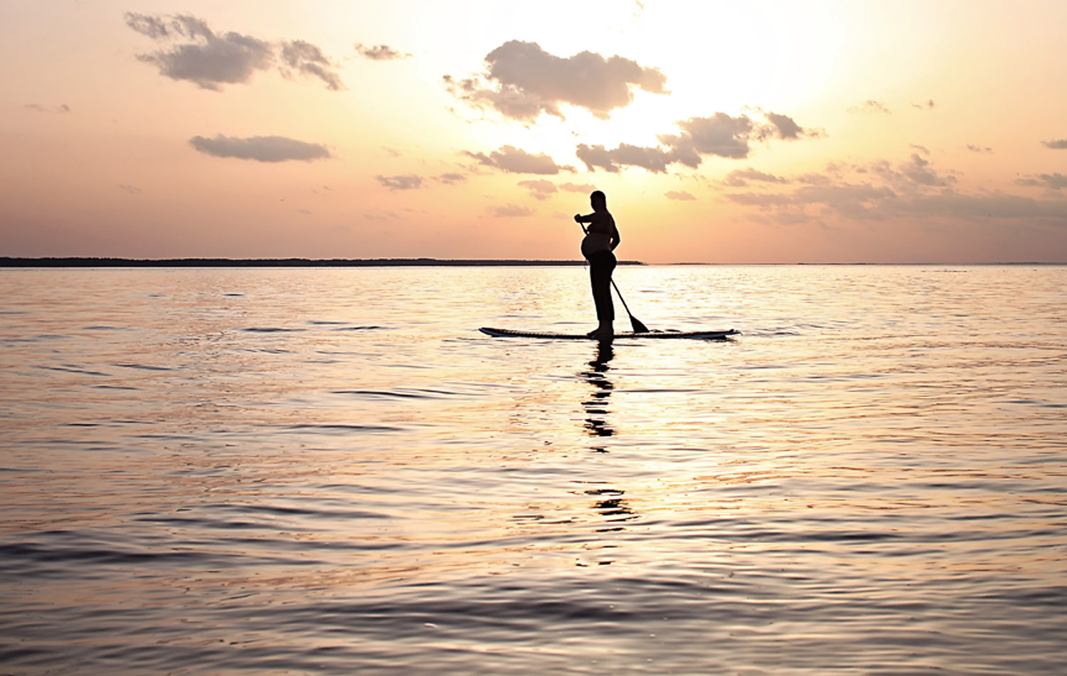 Pregnant woman stand up paddle boarding at sunset in OBX NC
